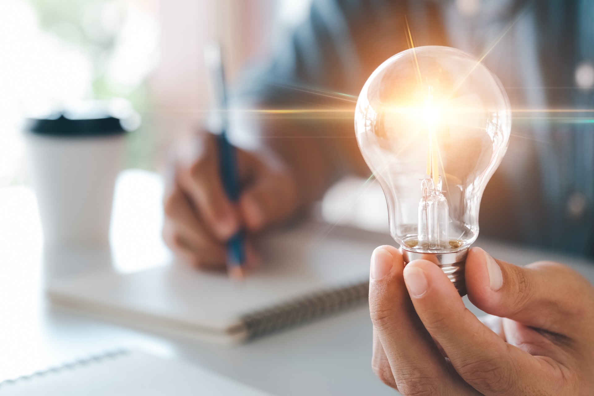 coaching Innovation through ideas and inspiration ideas. Human hand holding light bulb to illuminate, idea of creativity and inspiration concept of sustainable business development.